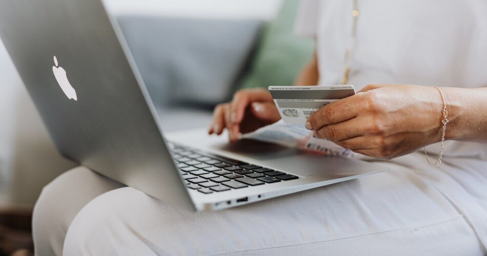 person using a macbook and holding a credit card