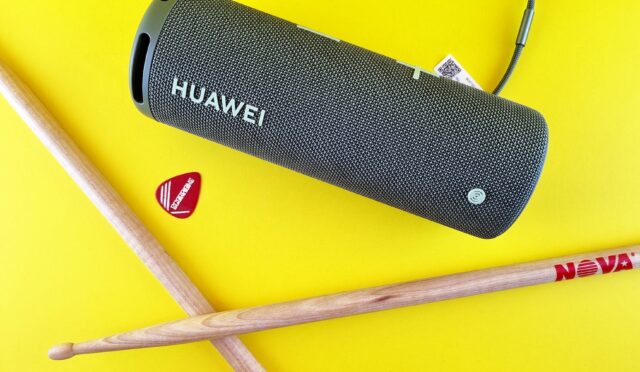 a guitar pick drumsticks and portable speaker on a yellow surface